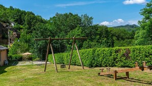 Un ensemble de balançoires en bois installé dans un espace herbeux, avec une haie et des arbres en arrière-plan.