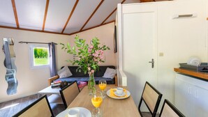 Un coin repas avec une table dressée pour deux personnes, un vase rempli de fleurs et une vue sur un jardin par la fenêtre.
