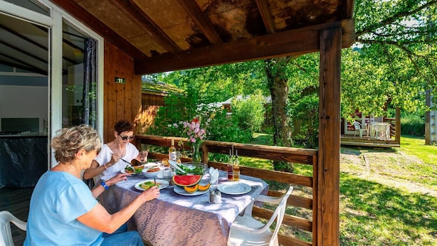 A covered outdoor dining area with a wooden deck, a table set with plates, glasses, and a watermelon centerpiece.