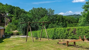 A wooden swing set in a grassy area with a hedge and trees in the background.