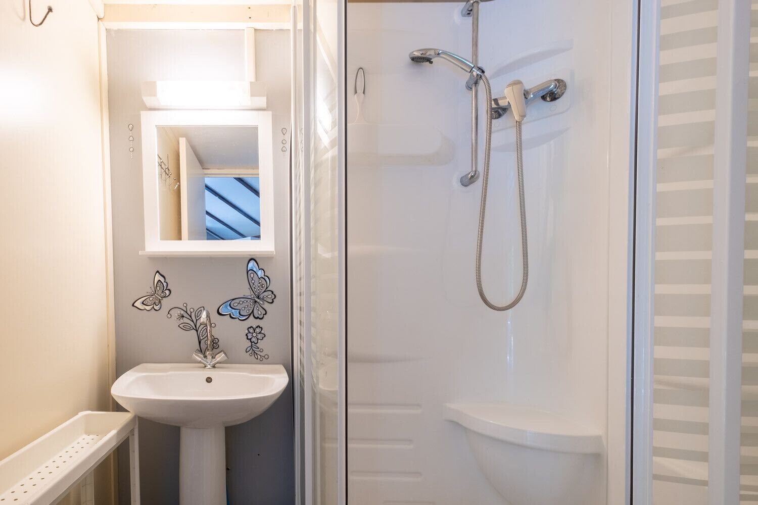 A bathroom with a white sink, a glass shower enclosure, and decorative butterfly wall decals.