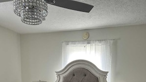 A bedroom with a large bed, two bedside tables, a chandelier, and a window with curtains.