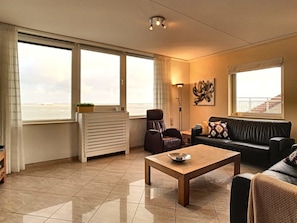 A spacious living room with a large window, a sofa, a coffee table, and a radiator.