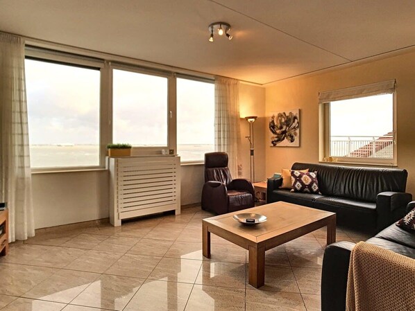 A spacious living room with a large window, a sofa, a coffee table, and a radiator.