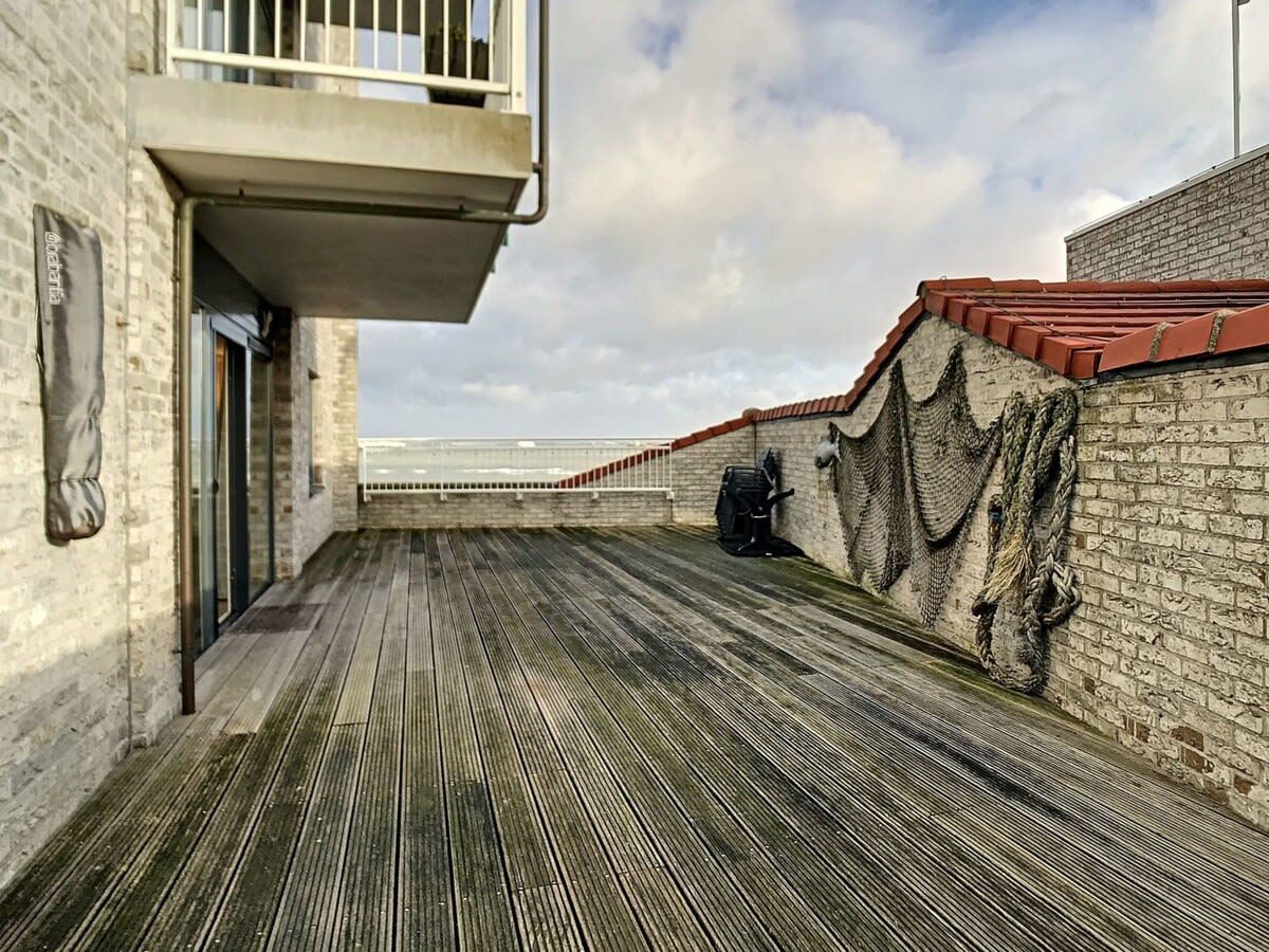 Eine Holzterrasse mit einer Backsteinmauer und Geländer, die zu einem Balkon mit Meerblick führt.