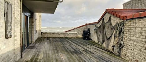 A wooden deck with a brick wall and a railing, leading to a balcony with a view of the sea.
