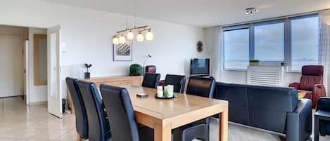 Un salon moderne avec une table à manger, des chaises noires, un canapé et un téléviseur.