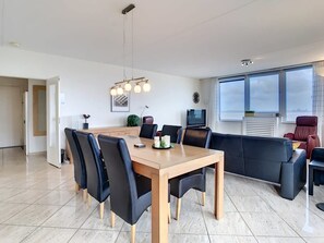Una sala de estar moderna con una mesa de comedor, sillas negras, un sofá y un televisor.