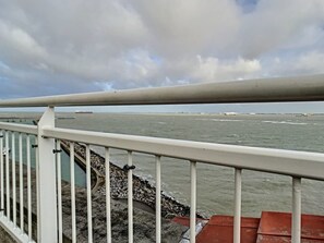 Vista costera desde un balcón con barandilla, que da sobre una costa rocosa y el mar.