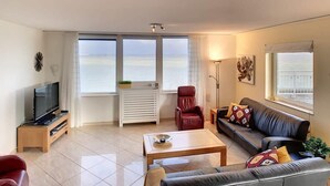 Een moderne woonkamer met een televisie, een leren bank en een rode fauteuil.