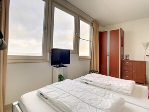 Habitación de hotel con dos camas, televisión, armario y ventana con cortinas.
