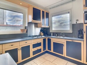Una cocina moderna con armarios de madera clara, estufa de acero inoxidable y un amplio ventanal.