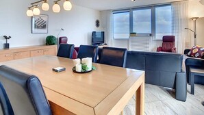 Een moderne hotelkamer met een houten eettafel, zwarte leren stoelen, een bank en een televisie.