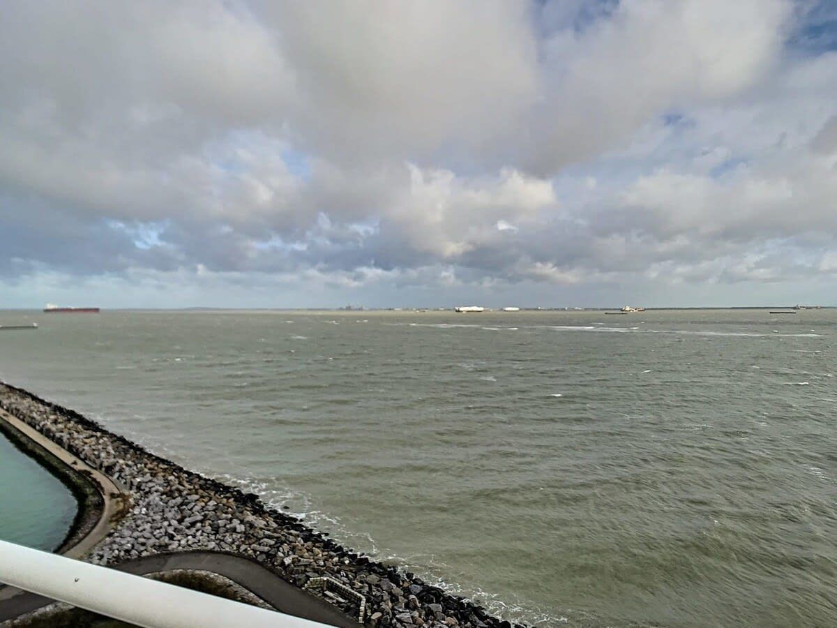 A view of a body of water with a rocky breakwater and distant ships.