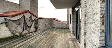 Una terraza en la azotea con piso de madera, paredes de ladrillo y techo rojo.