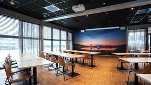 Suuriin ikkunoihin, auringonlaskua kuvaavaan seinämaalaukseen sekä useisiin pöytiin ja tuoleihin varustettu kokoushuone.