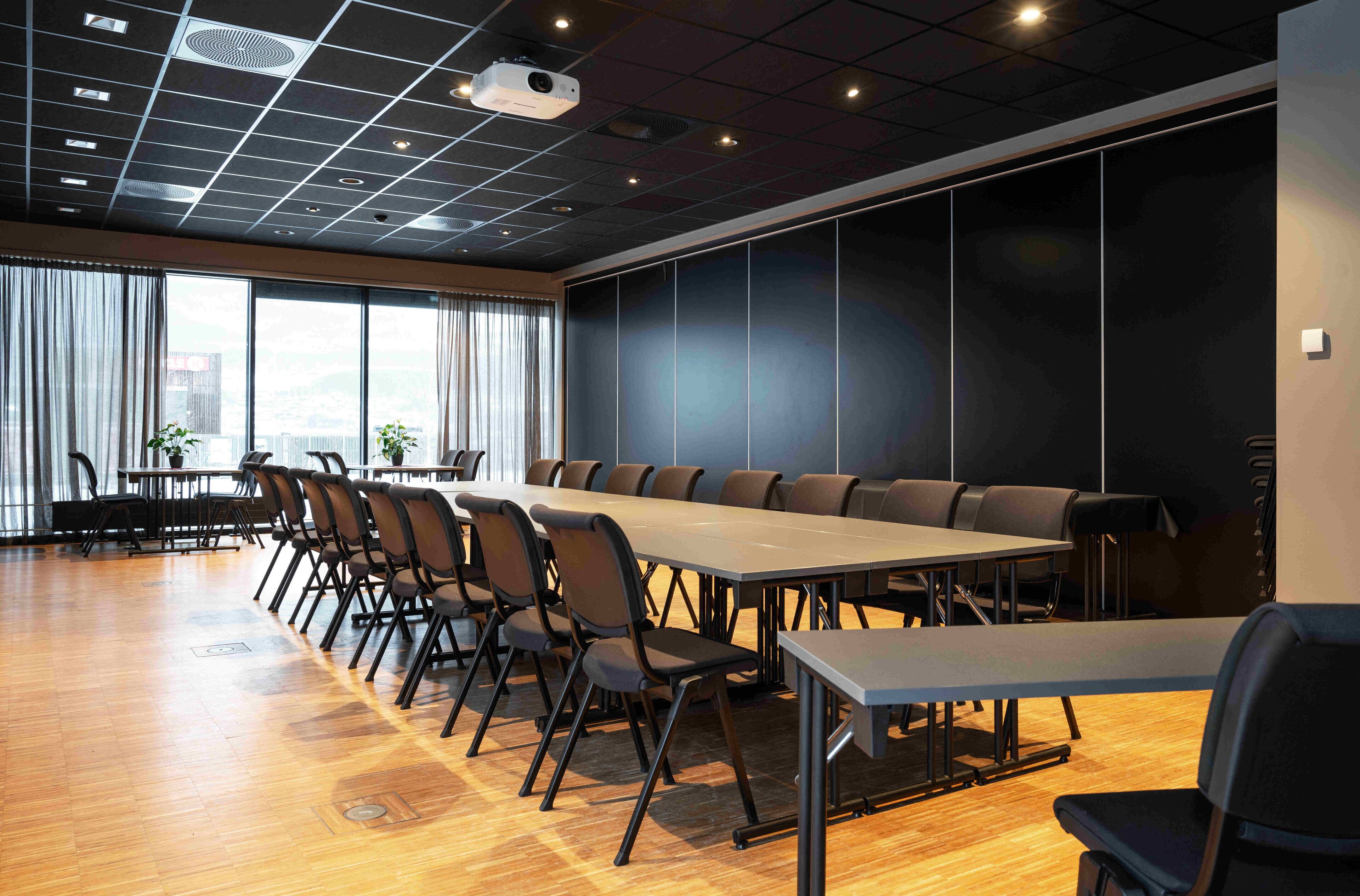 A conference room with a long table, chairs, and a projector on the ceiling.
