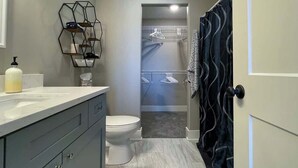 A bathroom with a toilet, a shower, a vanity with a mirror, and a towel rack. - Charming 3 bedroom Condo in Bettendorf with King Master Suite (Bettendorf)