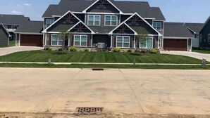 A two-story house with a symmetrical facade, a central entrance, and a driveway leading to a garage. - Charming 3 bedroom Condo in Bettendorf with King Master Suite (Bettendorf)