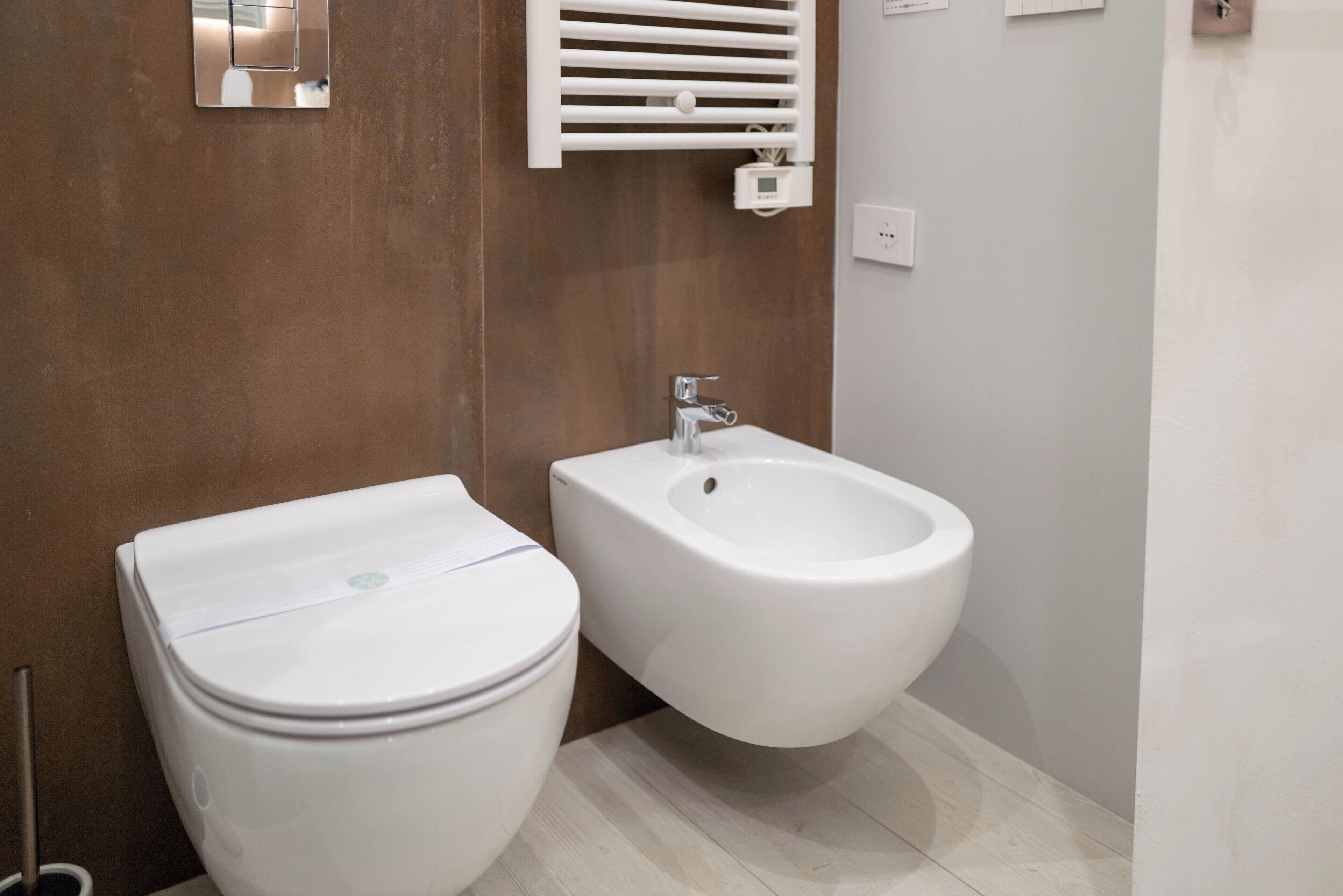 Un bagno moderno con servizi igienici, bidet, rivestimenti in legno e pavimento chiaro.