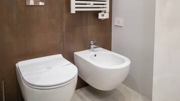 Un bagno moderno con servizi igienici, bidet, rivestimenti in legno e pavimento chiaro.
