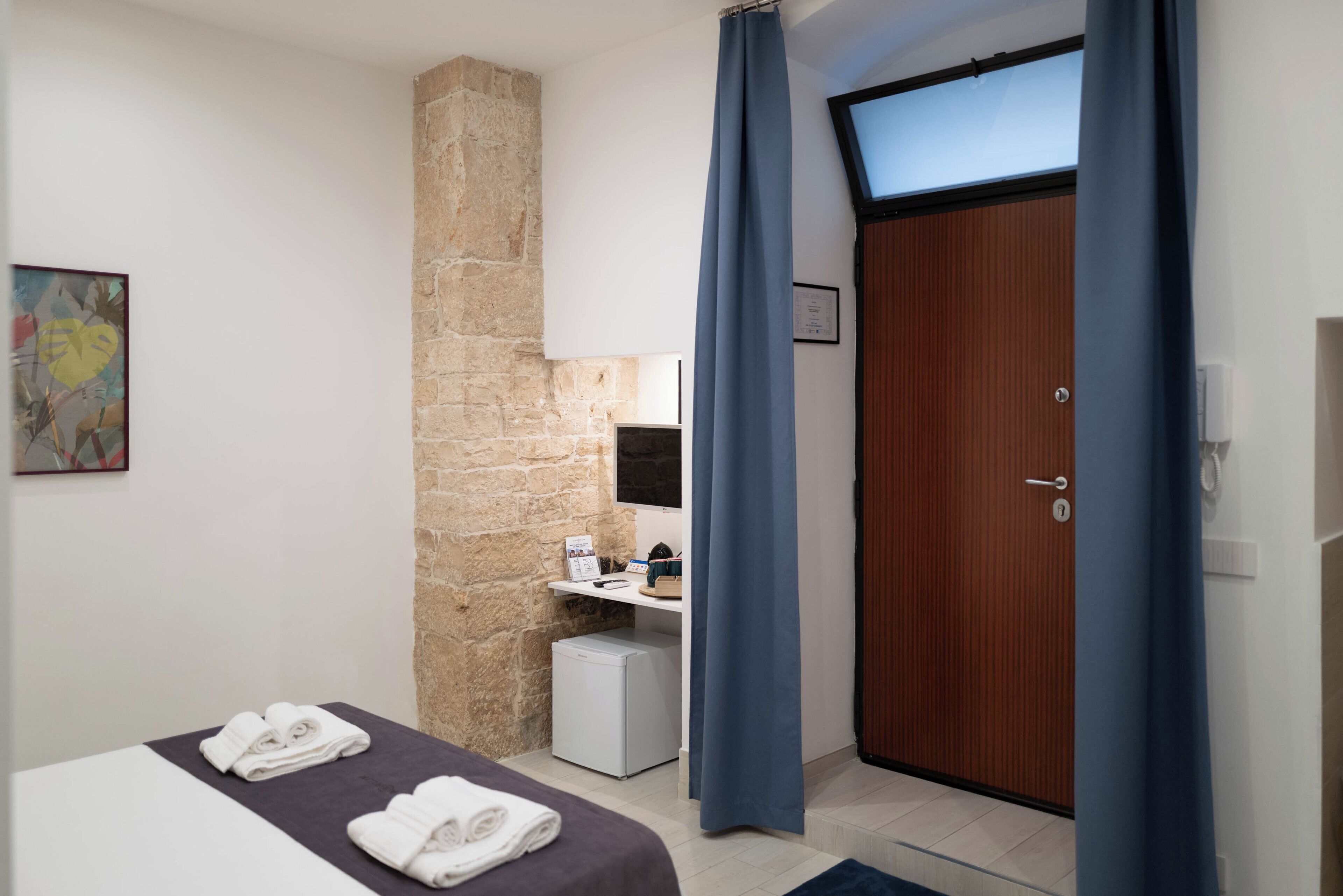 Habitación de hotel con cama, un escritorio pequeño, pared de piedra, puerta de madera y ventana con cortinas.