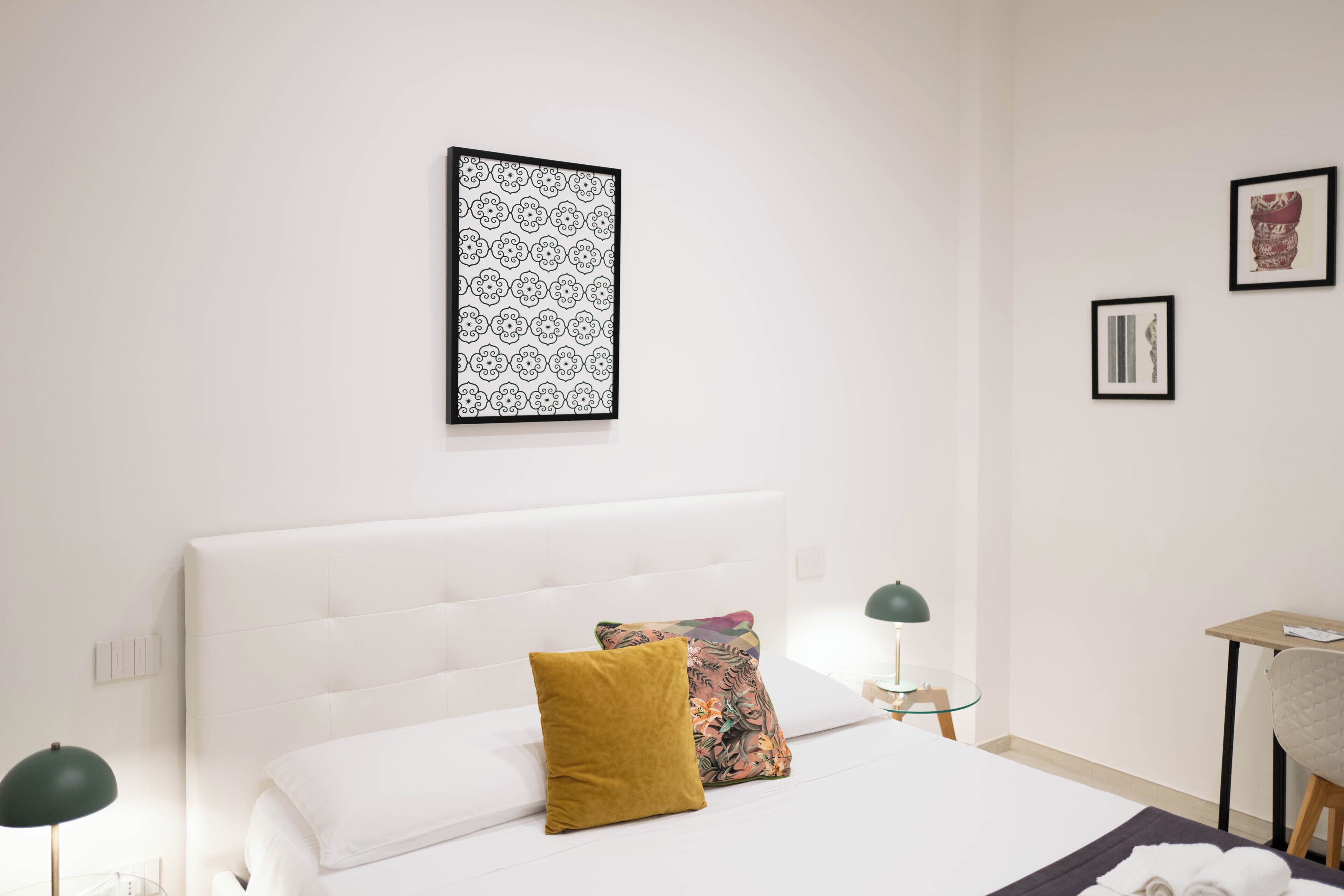 Una habitación de hotel con una cama grande, dos almohadas, una obra de arte enmarcada, una mesita con una lámpara y una silla.