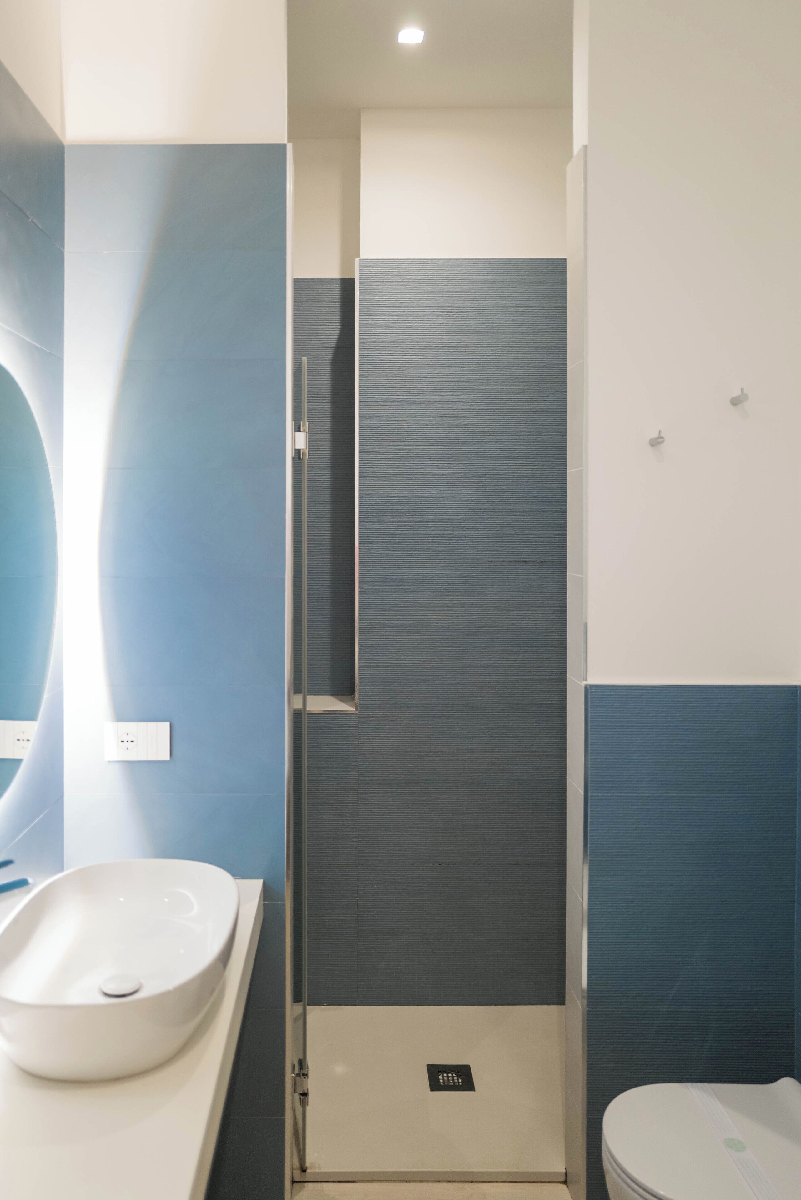Un baño moderno con un espejo grande, un lavamanos blanco, una cabina de ducha con mampara de cristal y un inodoro.