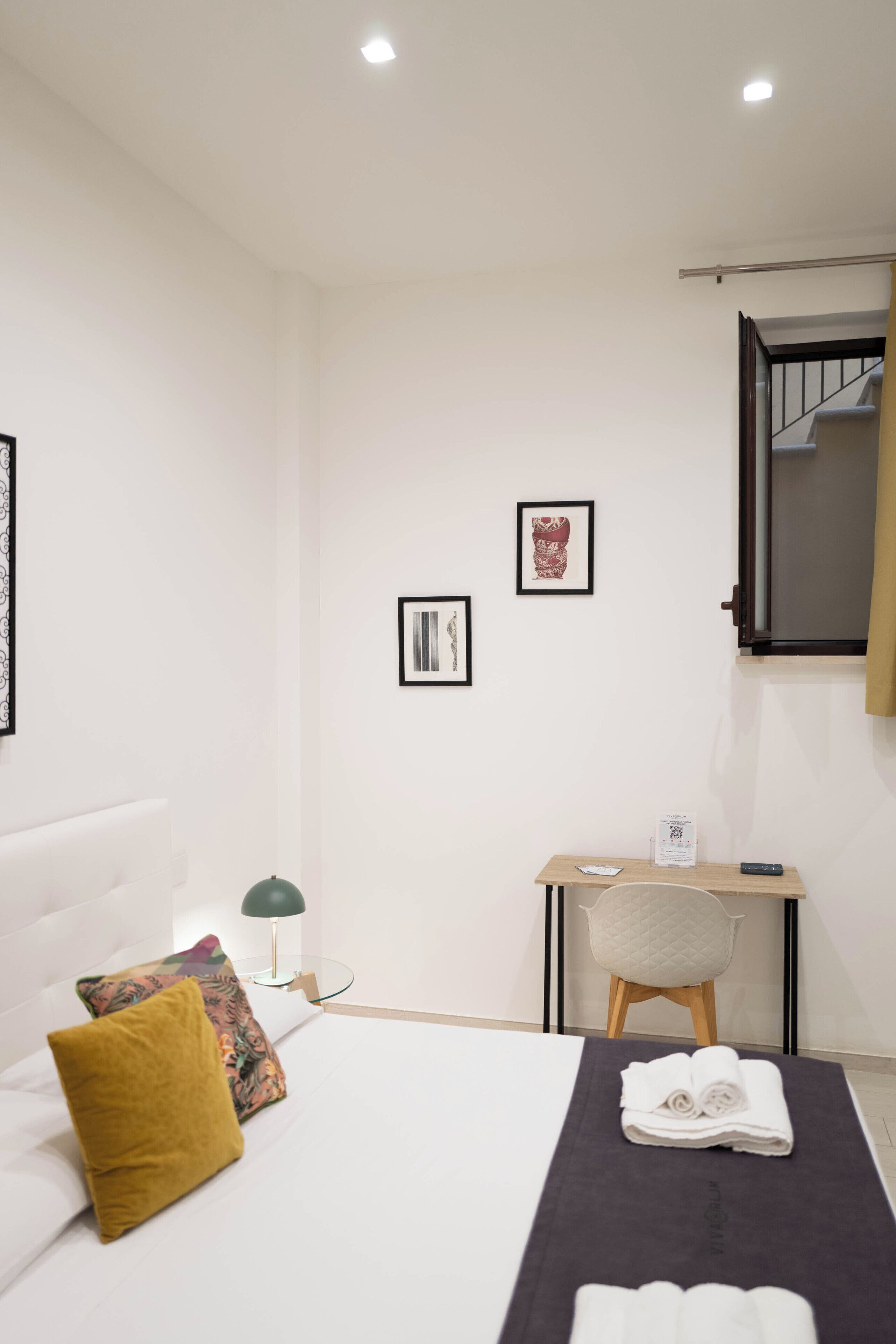 A hotel room with a bed, a desk, a chair, and a small table with a remote control.