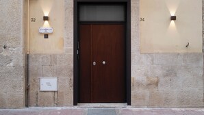 Uma porta dupla de madeira com um painel de vidro acima, acompanhada por dois apliques na parede e um interfone.