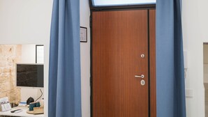 Um quarto com porta de madeira, uma pequena escrivaninha com um computador e uma parede de pedra.