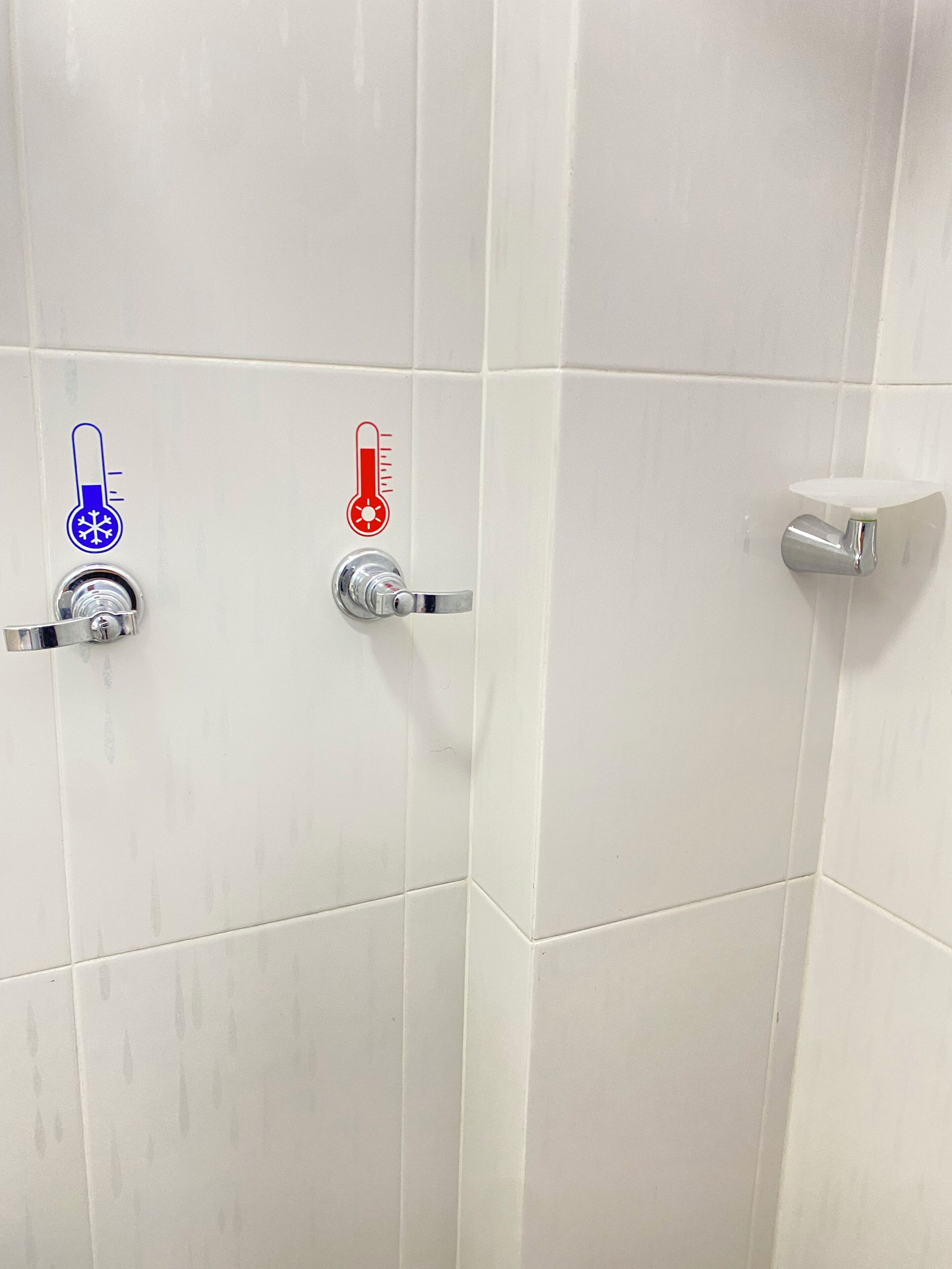 A bathroom with white tiled walls and two faucets, one with a blue and white temperature control and the other with a red and white temperature control.