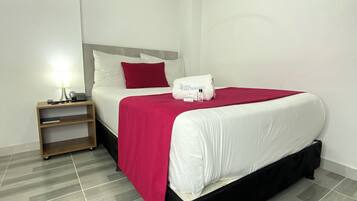 A hotel room with a bed, a nightstand with a lamp, and a red pillow.