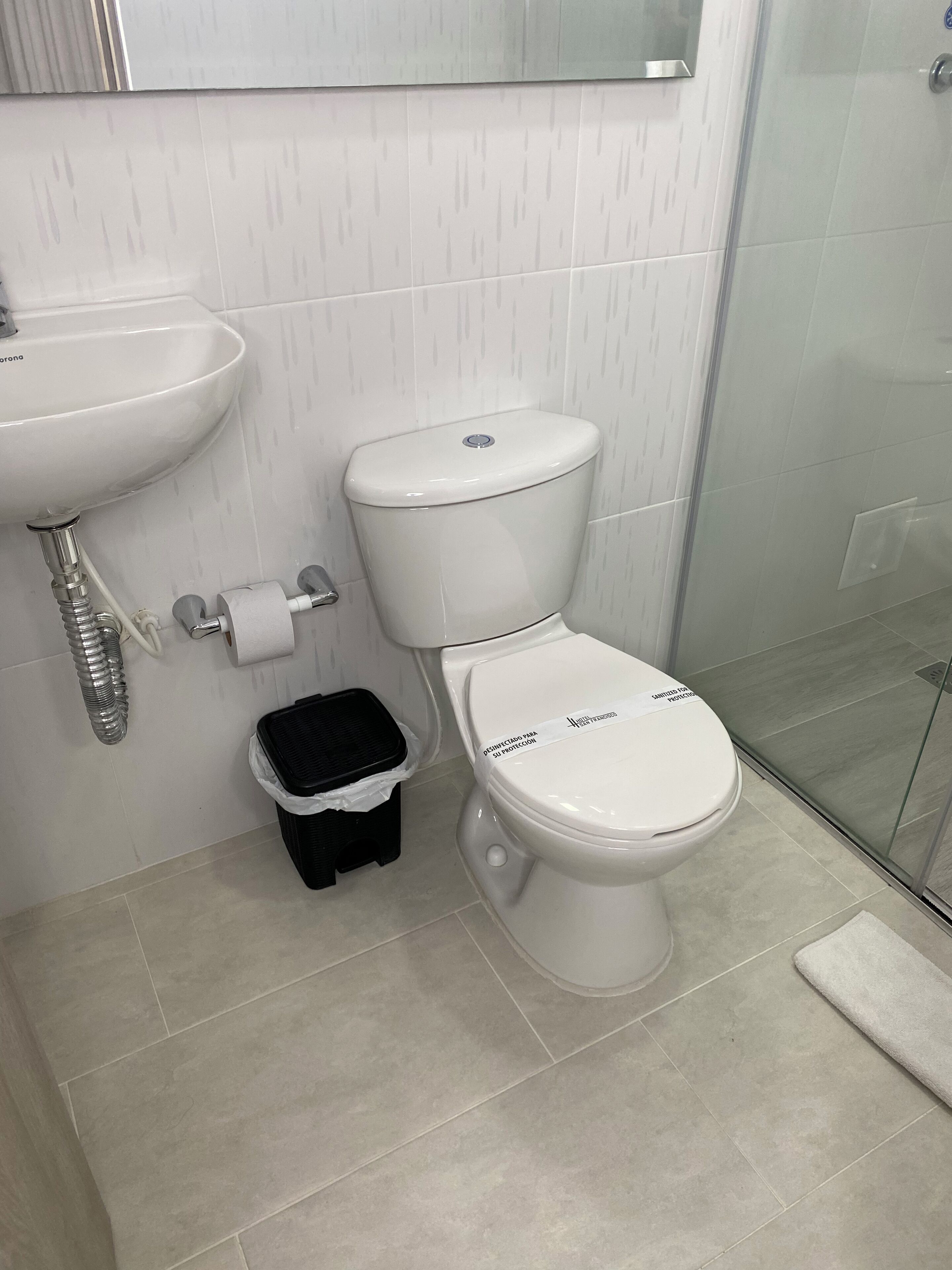 A bathroom with a white toilet, a sink, and a trash bin.