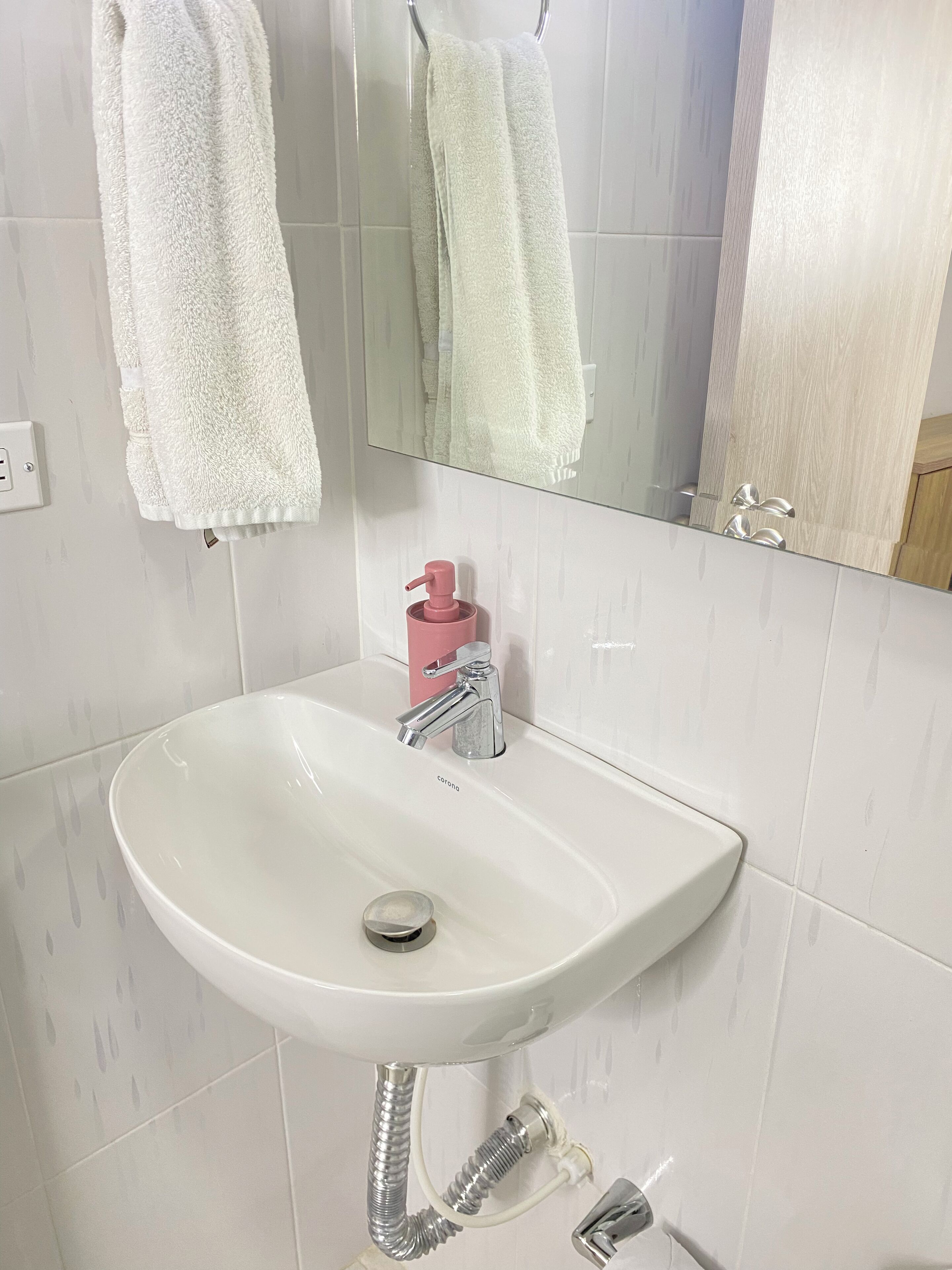 Un bagno con un lavandino bianco, uno specchio e due asciugamani appesi al muro.