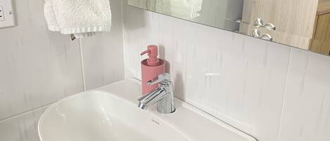 Un bagno con un lavandino bianco, uno specchio e due asciugamani appesi al muro.