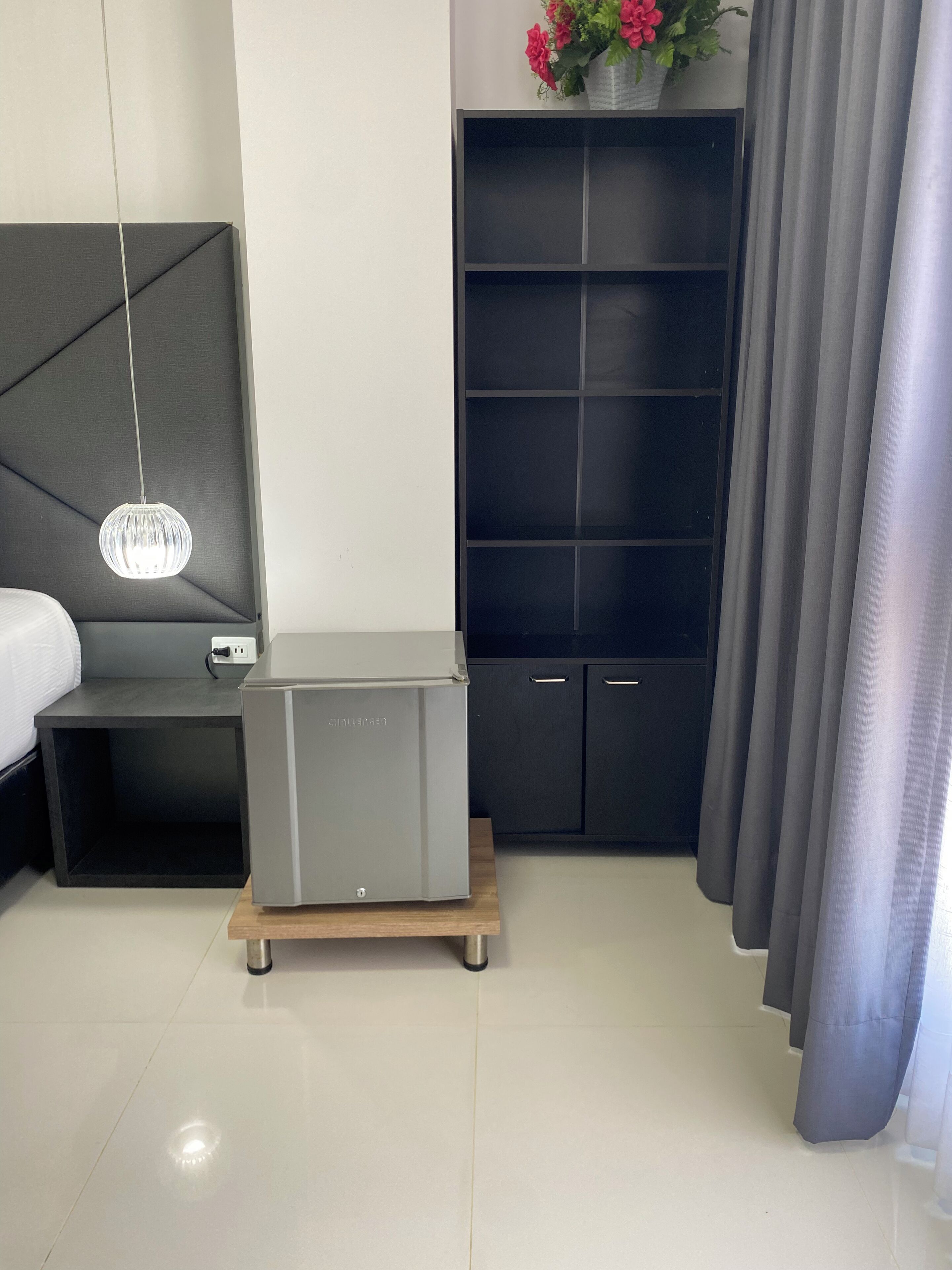 A modern bedroom with a bed, bedside table, a small desk, a wardrobe, and a hanging light fixture.