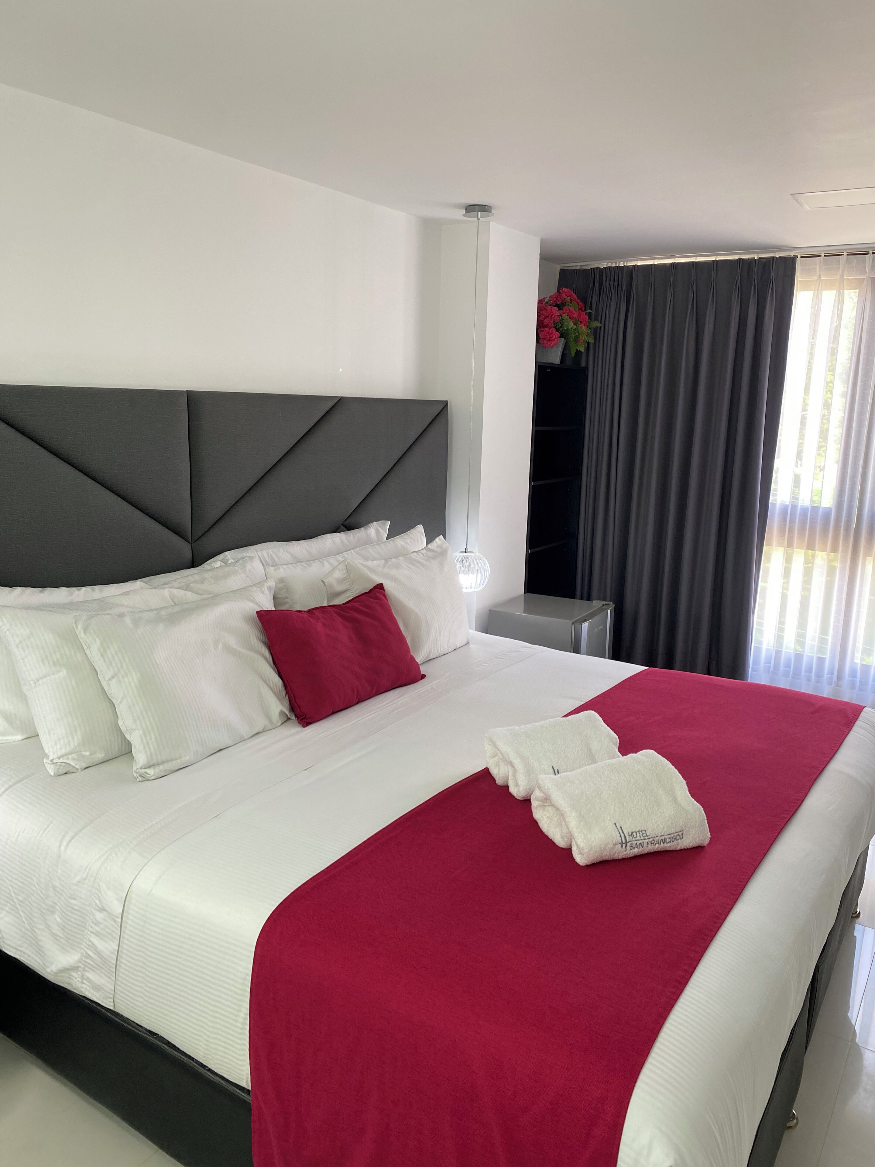 A modern hotel room with a large bed, white linens, a red throw blanket, and a grey headboard.