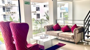 Een moderne woonkamer met een beige bank, rode fauteuils en een glazen salontafel.