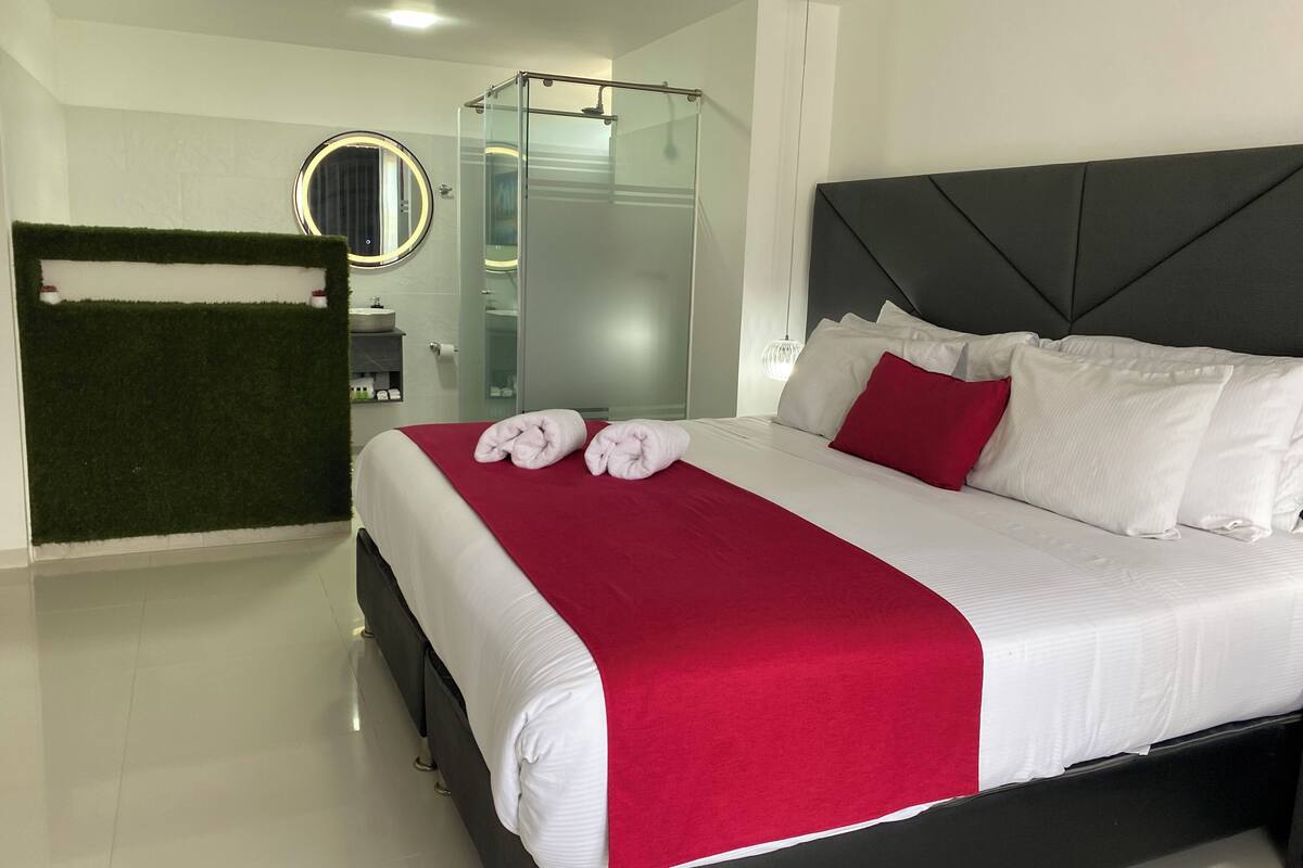 A modern hotel room with a large bed, a glass shower enclosure, and a green wall.