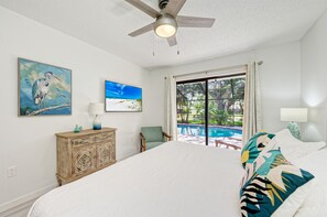 A bedroom with a bed, a ceiling fan, a window with a view of a pool, and artwork on the wall. - Heated Pool + Game Room + Free EV Charging near Anna Maria Island & IMG Academy (Bradenton)