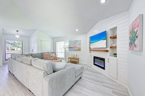 A modern living room with a sectional sofa, a fireplace, and artwork on the walls. - Heated Pool + Game Room + Free EV Charging near Anna Maria Island & IMG Academy (Bradenton)