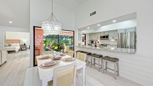 Una cocina moderna con electrodomésticos de acero inoxidable, una isla grande con taburetes y un comedor con mesa y sillas blancas.