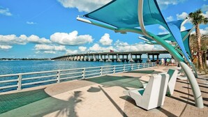 Un paseo marítimo con un puente moderno, zonas de estar y una palmera.