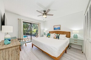 Een slaapkamer met een groot bed, een plafondventilator, een nachtkastje, een bureau en uitzicht op de omgeving.