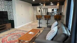 A modern living room with a sofa, a coffee table, a TV, and a kitchen area with bar stools. - Newly Renovated Downtown Gem! (Buffalo)