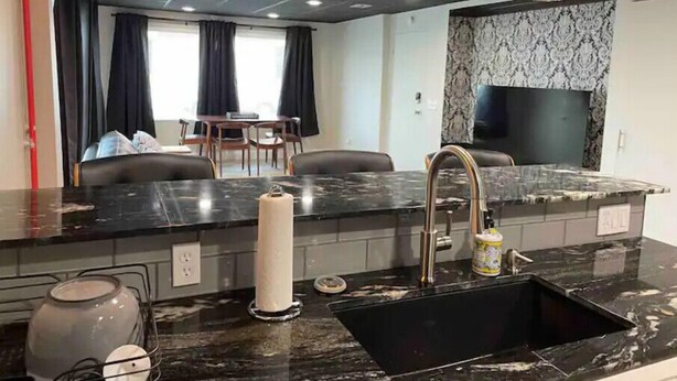A modern kitchen with a black marble countertop, stainless steel sink, and overhead lighting. - Newly Renovated Downtown Gem! (Buffalo)
