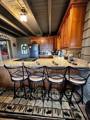 Une cuisine avec des meubles en bois, un plan de travail en granit et un îlot central intégré avec des tabourets de bar.