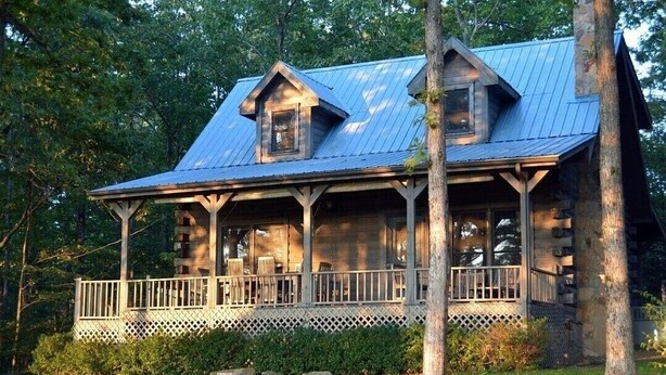 Une cabane rustique dotée d’une véranda, de poutres en bois et d’un toit en métal.