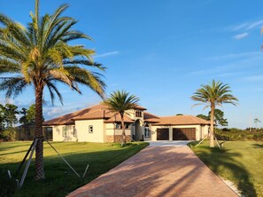 A single-story house with a tiled roof, a driveway, and palm trees. - Stunning Luxury Mediterranean-style Private Oasis! (Grant-Valkaria)